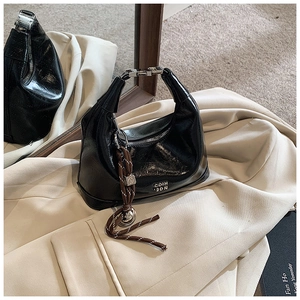 Detail of black glossy hobo bag with silver buckle and decorative woven pendant