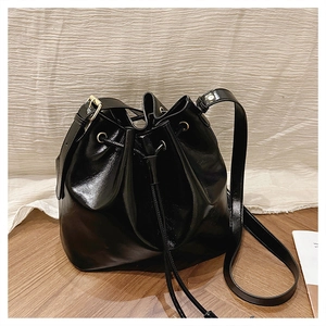 Détail d'un sac seau noir brillant avec des ferrures dorées et une fermeture à cordon
