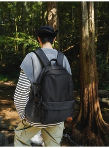 Rear view of a black nylon outdoor backpack with multi-layer zippers in a forest setting