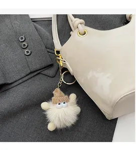 Detail of a plush monster bag charm with a beige fur ball and a small knitted hat