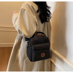 Model showing a black crossbody nylon bag with round logo patch and adjustable strap