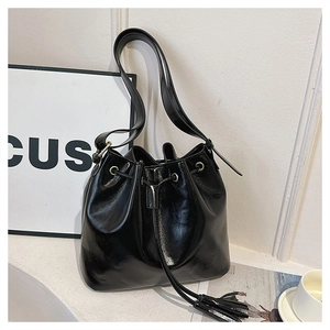 Détail du sac seau noir en cuir verni avec œillets dorés et cordon de serrage à glands