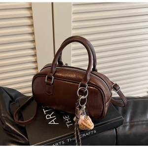 Gros plan du sac Boston marron rétro avec texture cuir et breloque baseball sur livre