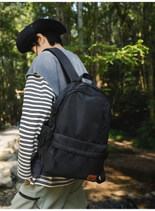 Outdoor view of a black nylon backpack with orange leather label and side straps