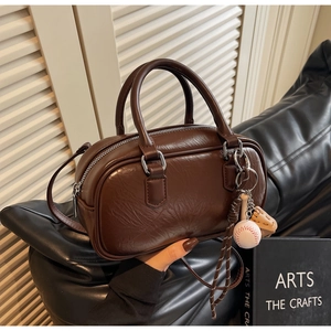 Détail du sac cylindre plissé marron foncé avec breloques de baseball et poignées
