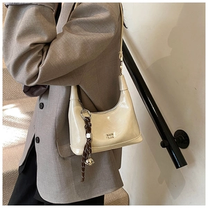 Detail of cream patent leather hobo bag with braided strap and silver bell charm