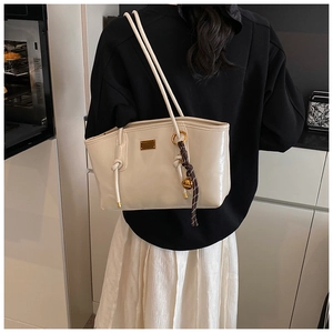 Detail of cream leather tote bag with gold metal plate and woven charm on a model's shoulder