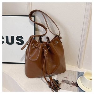 Détail d'un sac seau marron avec cordon de serrage, cuir brillant et longs glands