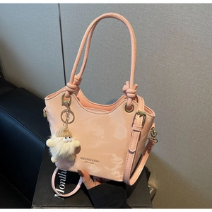 Detail of pink matte leather bucket bag with knot handles and cute plush monster charm