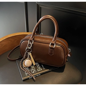 Détail d'un sac Boston en cuir marron foncé avec breloques de baseball et glands