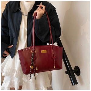 Detail of red glossy tote bag with gold logo plate and checkered woven charm on strap