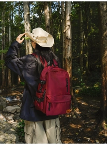 Detail view of burgundy waterproof nylon backpack with orange tag in a forest setting