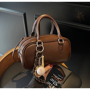 Détail d'un sac Boston en cuir marron avec pendentif baseball et décor de livre