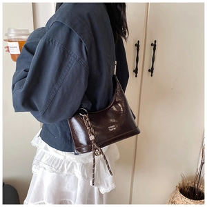 Close-up of brown polished leather hobo bag with woven tassel and shoulder strap detail