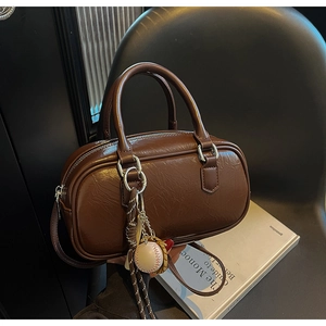 Détail d'un sac Boston rétro marron foncé avec pendentif baseball et pompon élégant