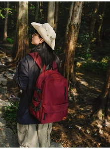 Burgundy casual backpack with adjustable side buckles shown in a forest setting