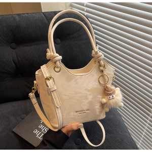 Détail du sac seau crème avec poignée nouée et breloque en peluche sur canapé