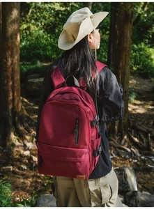 Close-up of a burgundy waterproof backpack with side buckle and leather brand tag