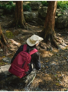Outdoor waterproof deep red backpack near forest stream with beige sun hat accessory