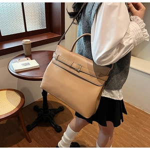 Detailed view of khaki leather tote bag with buckle strap on a model in a cafe setting