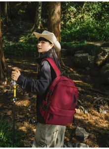Deep red outdoor backpack with side buckles and leather patch shown in a forest setting