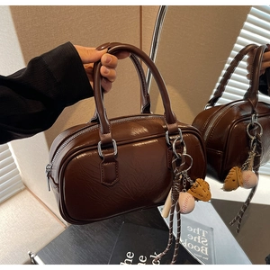 Détail du sac Boston en cuir marron foncé avec breloque de baseball et zip argenté