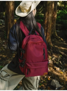 Outdoor shot of a durable burgundy backpack showing side strap details and fabric texture