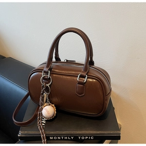 Détail d'un sac Boston en cuir marron avec fermeture éclair et breloque de baseball