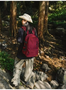Outdoor model wearing a dark red durable nylon backpack near a mountain stream