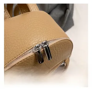 Close-up of premium camel leather texture and shiny silver dual metal zippers on backpack