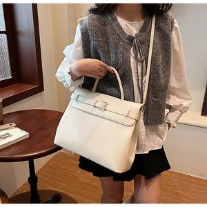 Detail of a large cream leather tote bag with metallic buckle and detachable shoulder strap