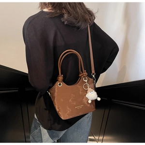 Detail view of brown leather bucket bag with knot handle and white plush charm on stairs