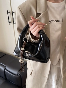 Fashionable black patent leather half-moon handbag with woven pendant and silver bell detail