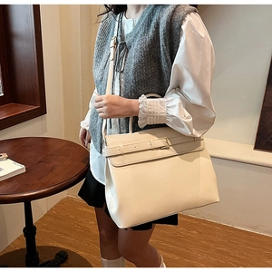 Lifestyle shot of a creamy white leather tote bag with decorative buckle and slim strap