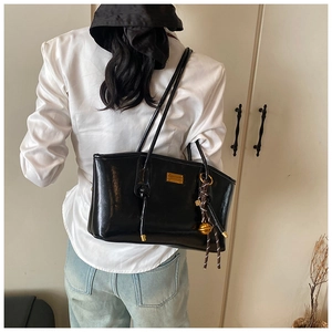 Detail of black glossy tote bag with gold logo and decorative striped tassel charm