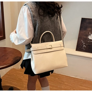Close-up of a beige trapezoid handbag showing the belt buckle and textured leather detail