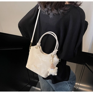 Detail of cream bucket bag with gold logo, knotted handle and fluffy monster charm