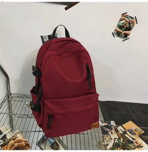 Detail view of burgundy waterproof nylon backpack with side buckle and brand logo