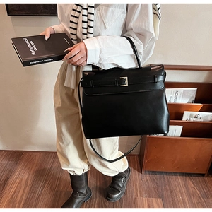 Detail of a large black vintage briefcase bag featuring a metal buckle and shoulder strap