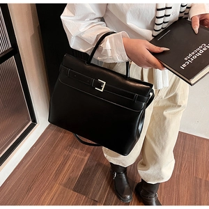 Detail of a vintage black leather briefcase featuring a gold metal buckle and strap