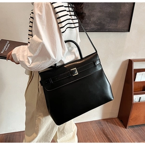 Detail of a large black leather tote bag with decorative metal buckle and long shoulder strap