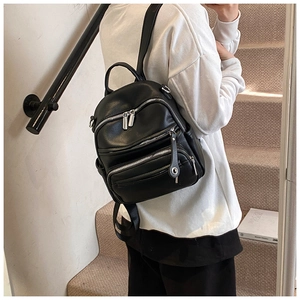 Detail of black pebbled leather backpack showing side pockets and silver zippers in use