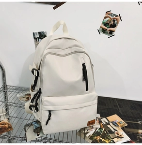 Detail of a beige canvas backpack with multi-pocket design and leather brand patch on a grid