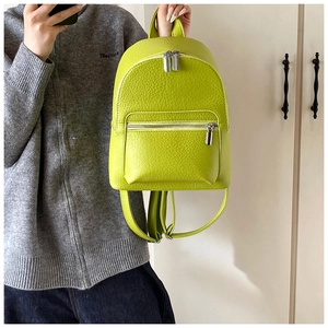 Detail of neon green mini backpack in pebble leather held by model for size comparison