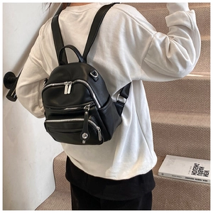 Lifestyle view of a black leather mini backpack on a model standing on indoor stairs