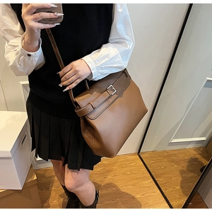 Brown leather satchel bag with buckle strap detail shown in a casual lifestyle setting
