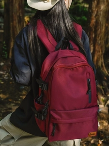 Burgundy high-capacity backpack shown from back view in a natural forest setting