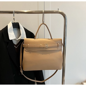 Detail of a beige professional briefcase bag hanging in an office setting with a suit