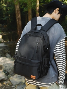 Black outdoor backpack with front zip pocket and buckle straps against forest background