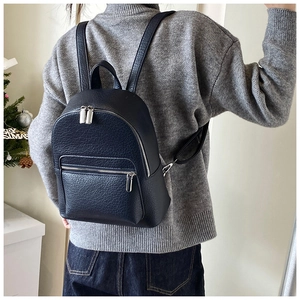 Rear view of a black pebbled leather mini backpack being worn in a stylish home setting